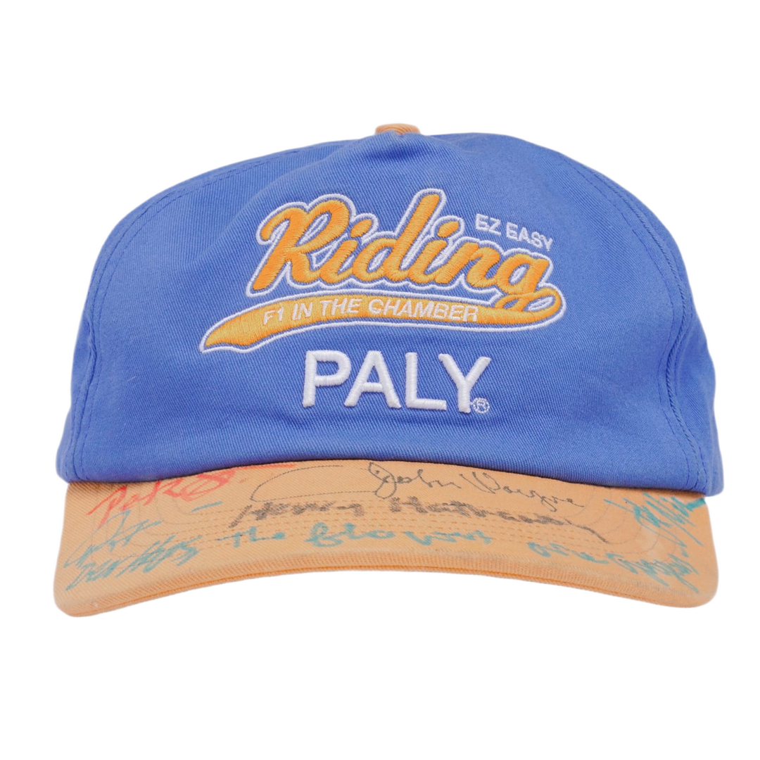 Front view of the Paly 'F1 Easy Riding' cap in a sun-faded cobalt blue cotton canvas, featuring bold orange and cream embroidered 'Riding' text above a clean cream-colored 'PALY' block logo, contrasted by a distressed cream-colored brim.