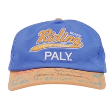 Front view of the Paly 'F1 Easy Riding' cap in a sun-faded cobalt blue cotton canvas, featuring bold orange and cream embroidered 'Riding' text above a clean cream-colored 'PALY' block logo, contrasted by a distressed cream-colored brim.