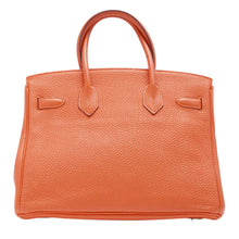 Back view of the orange grained leather Hermès Birkin 30 bag, showcasing the clean, seamless leather back construction and the precise stitching where the rear handles are anchored.