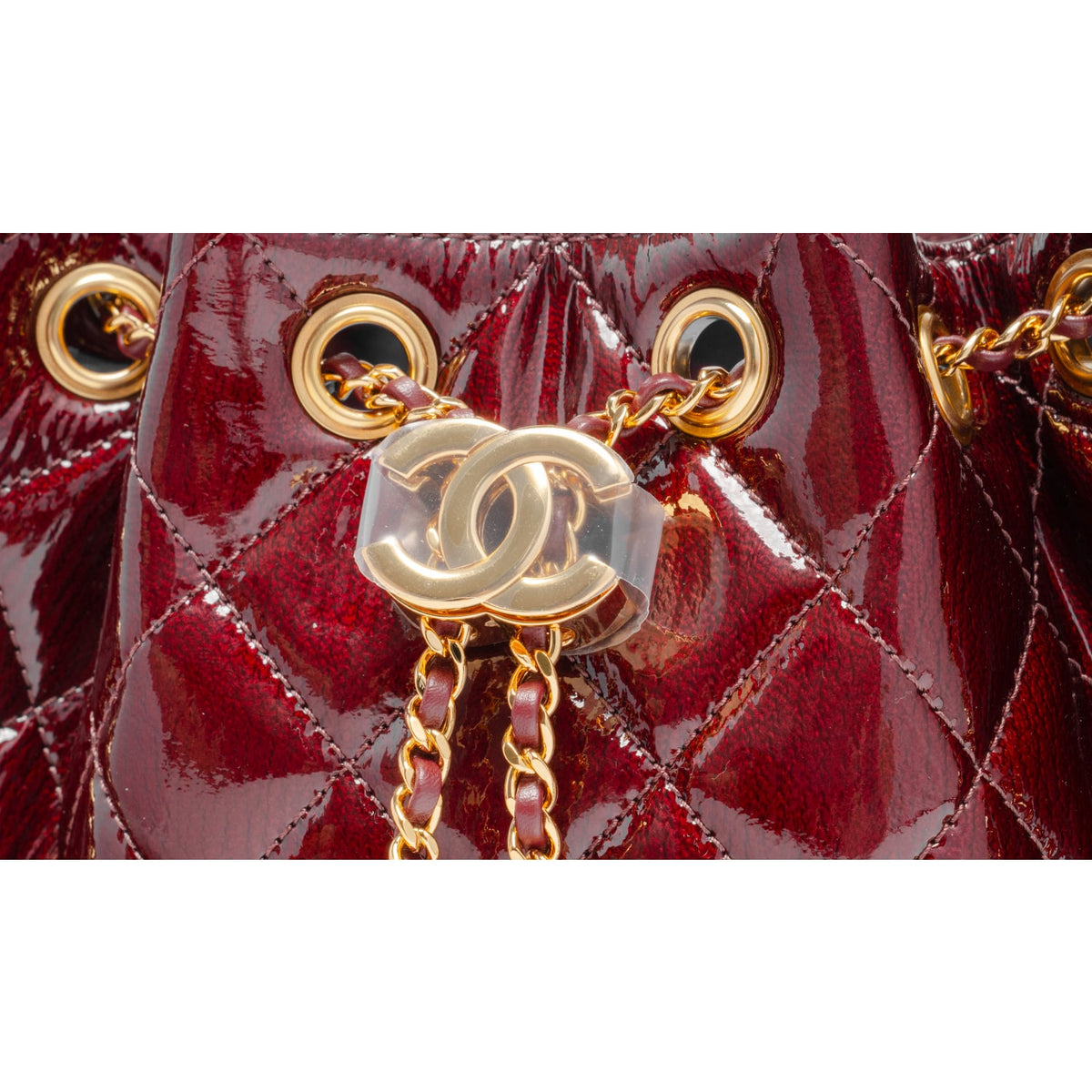 A macro close-up view focusing on the central closure, showcasing the meticulous detail of the polished gold-tone metal CC turn-lock clasp hardware mounted securely onto the crinkled burgundy diamond-quilted calfskin leather background.