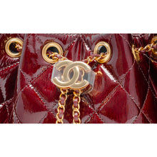 A macro close-up view focusing on the central closure, showcasing the meticulous detail of the polished gold-tone metal CC turn-lock clasp hardware mounted securely onto the crinkled burgundy diamond-quilted calfskin leather background.