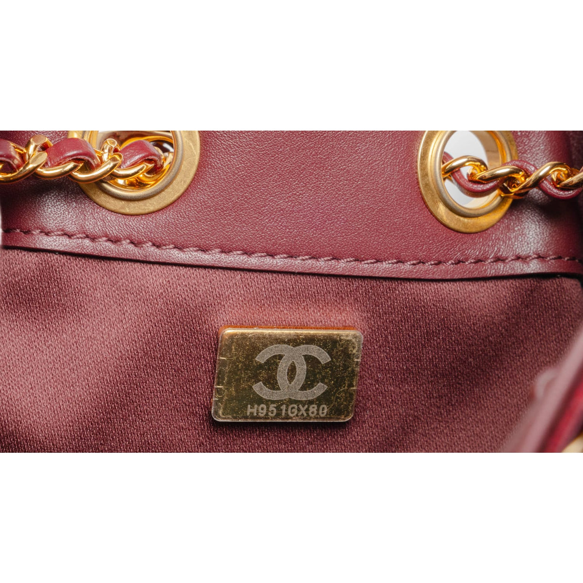 A detailed close-up shot focusing on the lower corner seam layout, showcasing the structural integrity of the curved piping borders, the high-gloss patina of the burgundy leather under studio lighting, and a glimpse of the gold chain anchor points.