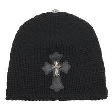 Front flat lay view of the Chrome Hearts beanie in a premium black cashmere knit, featuring a thick textured weave structure embellished with a large black leather cross patch centered on the front cuff and overlaid with a heavy sterling silver floral cross hardware centerpiece.