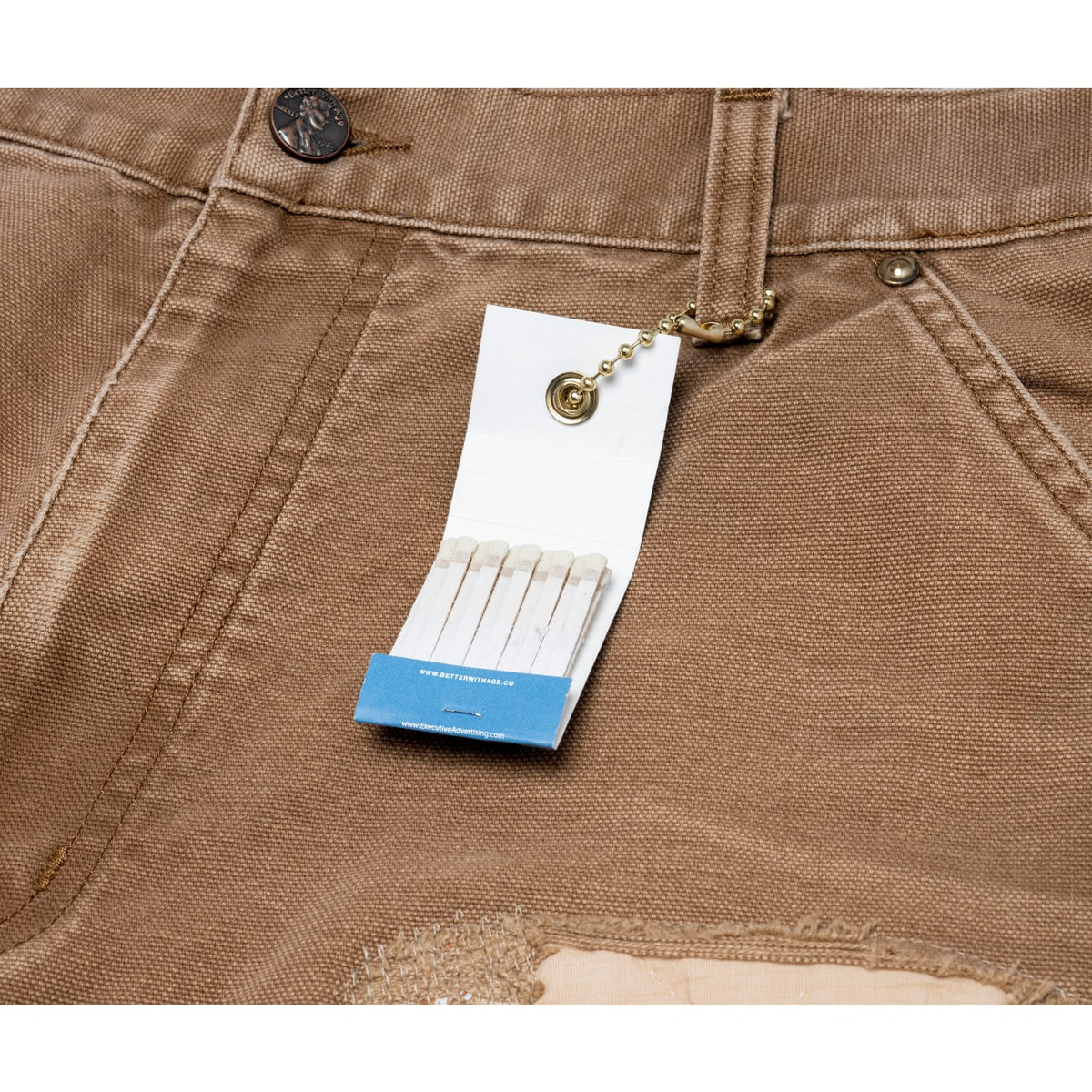 A detailed close-up view of the outer side seam, highlighting a functional white paper retail hangtag attached near the pocket, the thick canvas texture, and the clean edge geometry of the utility tool pocket construction.