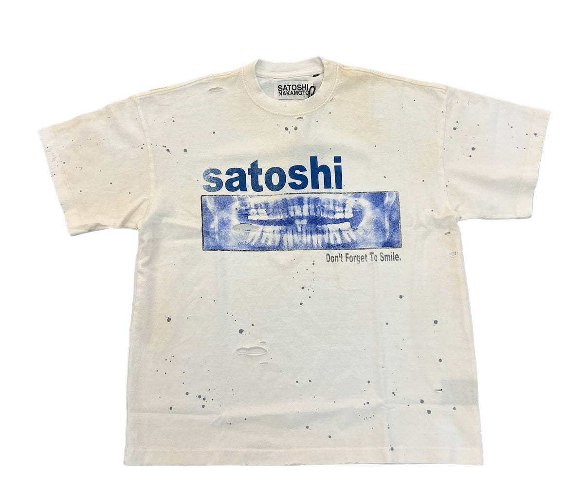 Front flat lay view of the Satoshi Nakamoto 'Don't Forget To Smile' short-sleeve t-shirt in a washed cream and grey tie-dye cotton, featuring heavy distressing with pinholes near the chest and hem, a large bright blue graphic print reading 'satoshi' across the center, and dark blue spray-paint style splatters.