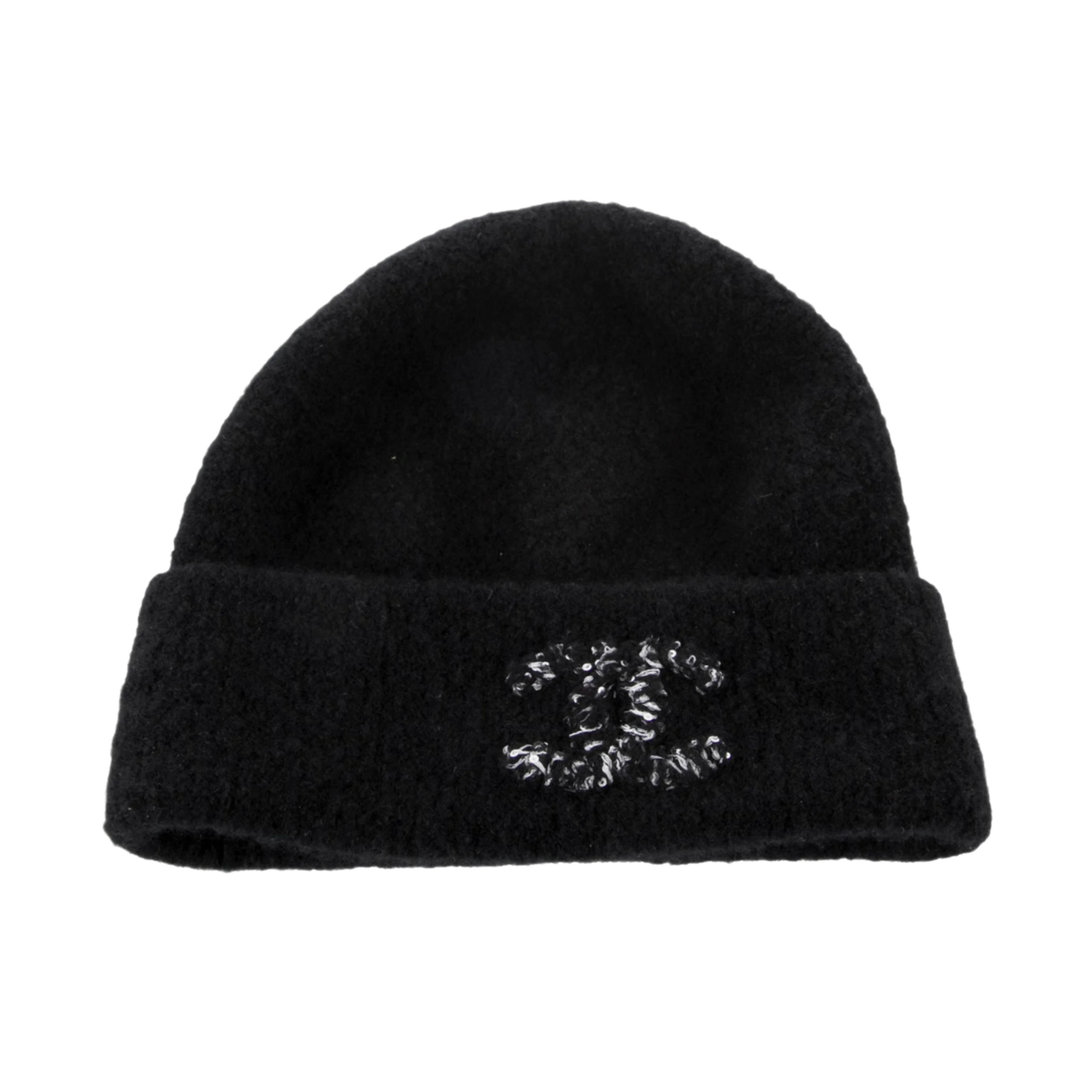Front flat lay view of the Chanel beanie in a premium black cashmere and silk blend, featuring a soft, fuzzy texture and a thick folded cuff embellished with a large interlocking CC logo crafted from thick black and white textured cotton yarn.
