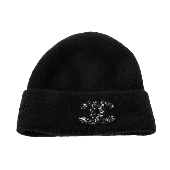 Front flat lay view of the Chanel beanie in a premium black cashmere and silk blend, featuring a soft, fuzzy texture and a thick folded cuff embellished with a large interlocking CC logo crafted from thick black and white textured cotton yarn.