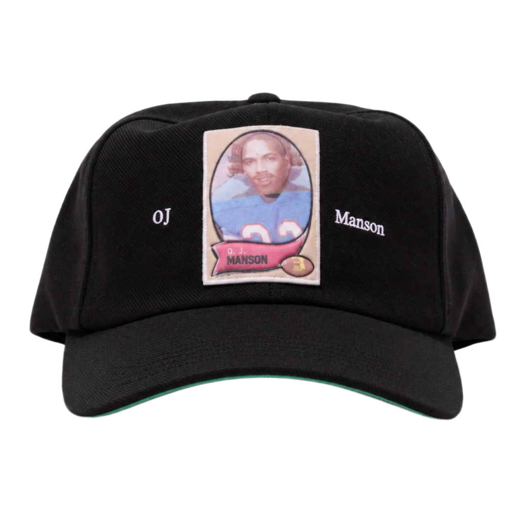 A straight front studio layout view of the Paly 'OJ Manson' hat, showcasing an unstructured six-panel vintage dad hat profile crafted from a premium washed jet-black cotton twill canvas, featuring a curved stitched brim, a centralized rectangular photo-graphic panel patch screen-printed on the front crown depicting an athletic sports trading card image, flanked on either side by minimal white printed script reading 'OJ' and 'Manson'.